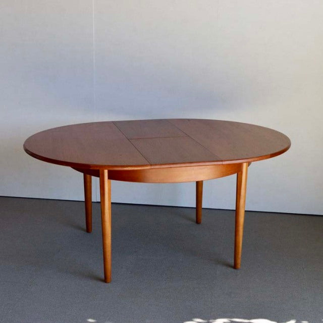 Mid-century British vintage teak round dining table with smooth wood grain and slender tapered legs.
