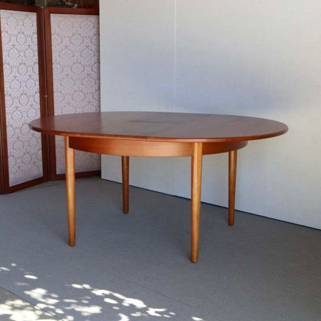 Vintage teak round dining table with tapered legs, British mid-century Danish design, smooth wood grain finish.