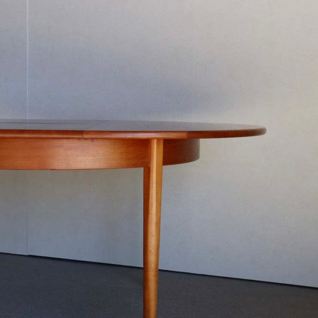 Mid-century British vintage teak round dining table with smooth wood grain and slender tapered legs.