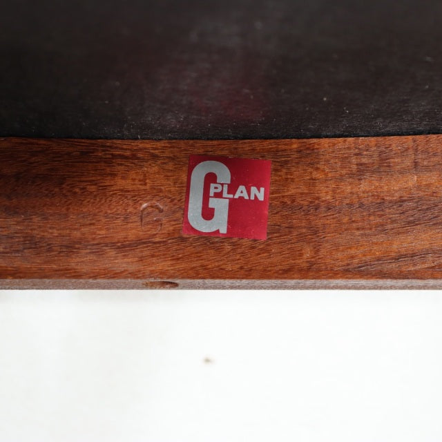 Close-up of rich teak wood grain with red and white G-Plan British mid-century vintage label on curved chair frame.