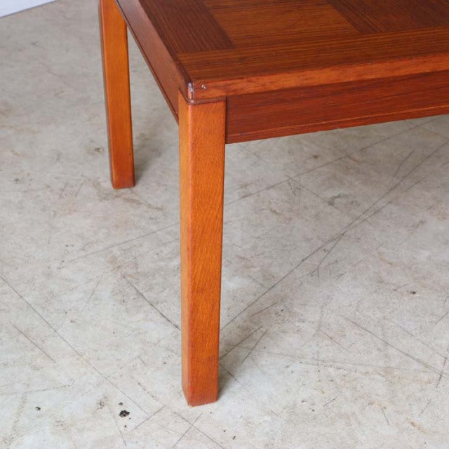 Mid-century British teak coffee table leg with warm rosewood grain and clean straight lines on concrete floor.