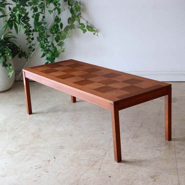 Mid-century Danish teak coffee table with checkerboard wood grain top and slender angled legs in vintage British style.