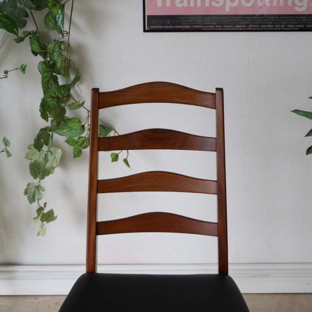 Set of four British mid-century G-Plan ladder back dining chairs in vintage teak with curved slats and black cushioned seats.
