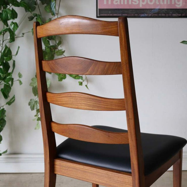Set of four vintage G-Plan ladder back dining chairs in teak with curved slats and black cushioned seats, mid-century.