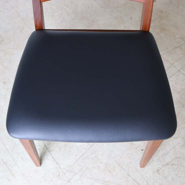 Set of four vintage mid-century British G-Plan dining chairs in teak with black leather seats and clean wood grain on ladder .