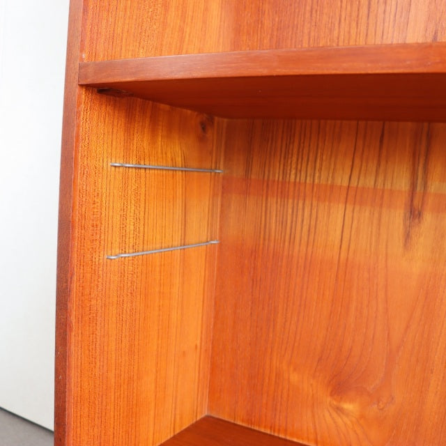 Vintage teak shelving unit corner with rich wood grain and slender iron support rods, mid-century Denmark design.