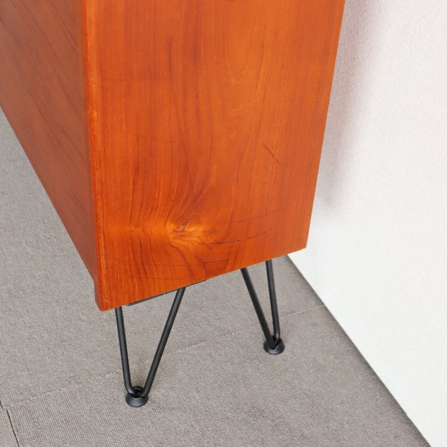 Mid-century vintage teak cabinet corner with smooth grain and black iron legs, Danish design detailing.