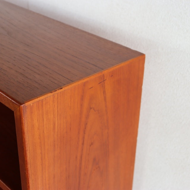 Vintage mid-century teak cabinet corner with smooth grain and warm honey tones against a light wall.