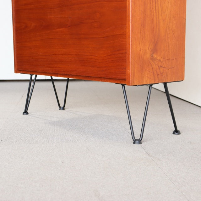 Vintage teak cabinet with smooth wood grain and slender black iron hairpin legs, mid-century Denmark design.