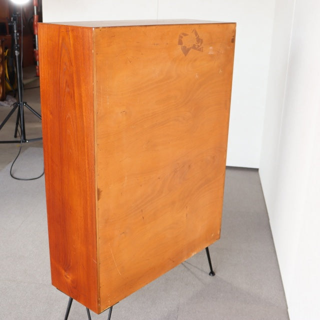 Vintage mid-century Danish teak cabinet with rich wood grain and slender black iron legs against white wall.