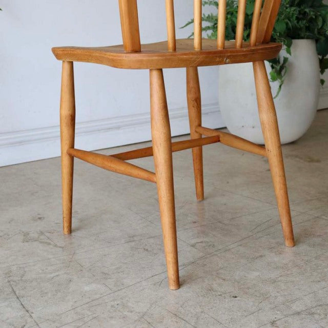 Mid-century British vintage Ercol dining chair in warm teak with slender spindle back and gracefully tapered legs showing.