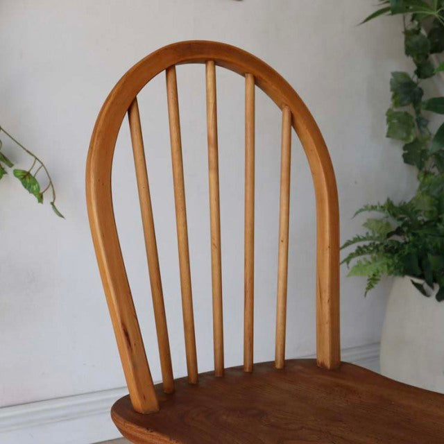Vintage British mid-century Ercol teak dining chair with smooth curved hoop back and vertical spindles, warm wood grain.