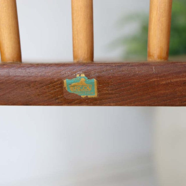 Close-up of mid-century British vintage Ercol chair backrest with warm teak wood grain and original green and gold label on.