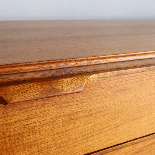 Close-up of vintage mid-century British teak sideboard drawer with smooth wood grain and curved integrated handle.