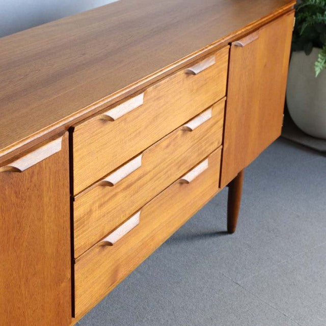 Vintage mid-century teak sideboard by Austinsuite featuring three drawers with recessed handles, tapered legs, and a smooth.
