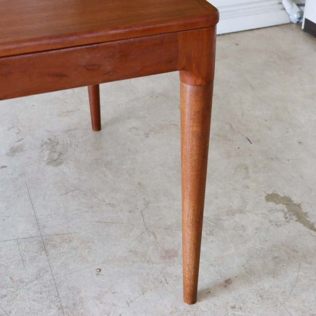 Mid-century vintage Danish teak dining table corner with smooth wood grain and tapered cylindrical leg.
