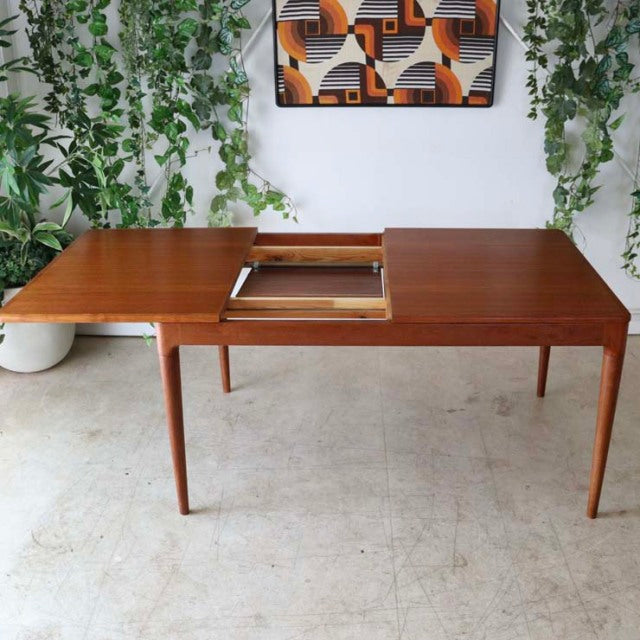 Mid-century vintage teak dining table from Denmark with rectangular top, tapered legs, and extension leaf mechanism visible.