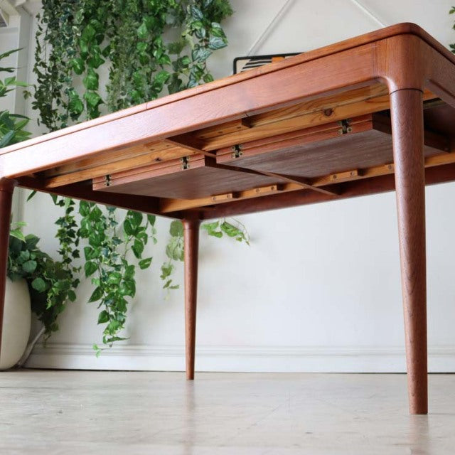 Mid-century vintage teak dining table from Denmark with rounded edges, slender tapered legs, and visible wood grain under a.