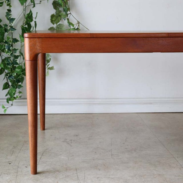 Mid-century Danish teak dining table with rounded corners, slender tapered legs, and warm wood grain finish.