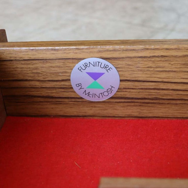 Round McIntosh label on teak wood with visible grain, vintage mid-century British furniture detail.