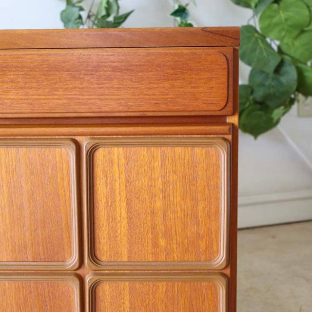 Mid-century British McIntosh vintage teak sideboard with rich wood grain and rounded cabinet doors against green foliage.