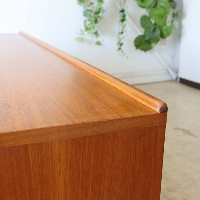 Close-up of vintage teak sideboard top with smooth wood grain and rounded edge, mid-century British-Denmark design.