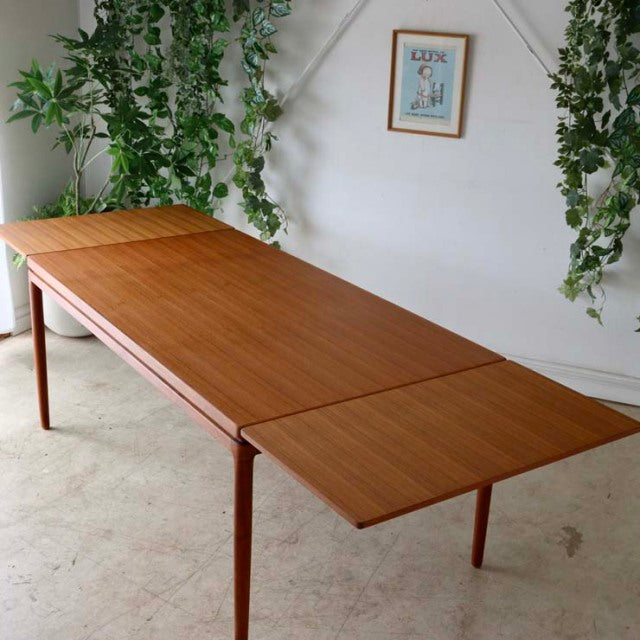 Mid-century vintage teak dining table by Johannes Andersen with rectangular top, visible wood grain, and slender tapered.