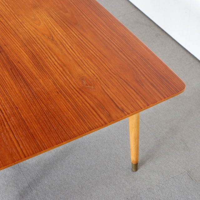Vintage mid-century teak coffee table corner with smooth wood grain and slender British-inspired tapered legs with brass caps.