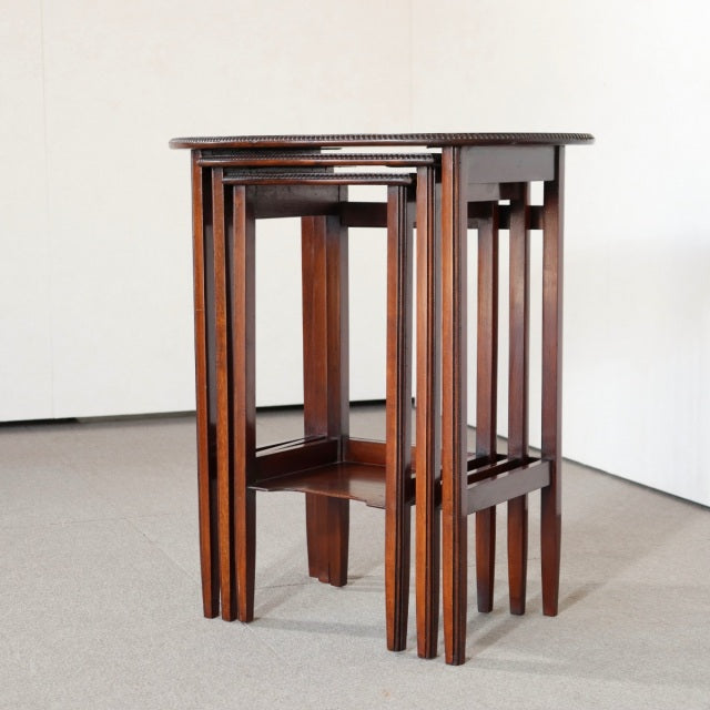 Set of three vintage teak British mid-century nest tables with slender tapered legs and visible wood grain.