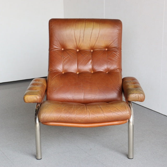 Mid-century vintage British leather sofa with teak armrests and metal legs, tufted backrest, rich caramel patina.
