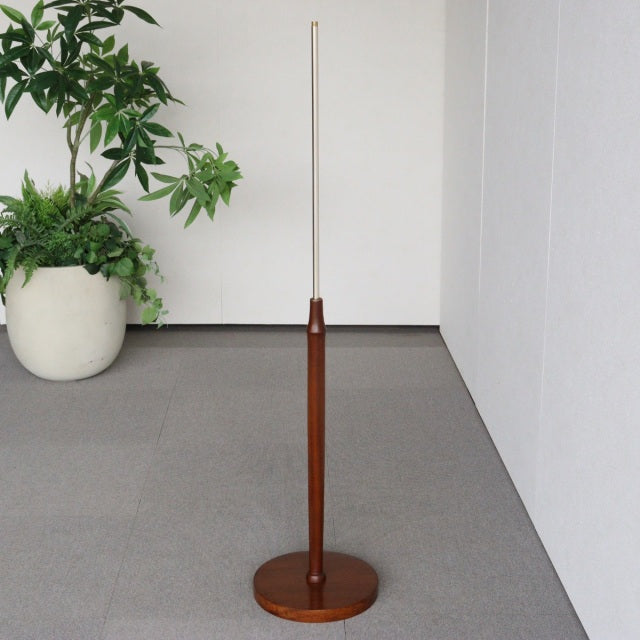 Mid-century British vintage teak floor lamp with slender wooden base and thin metal rod stem against white wall and gray.