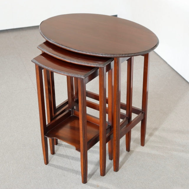 Set of three vintage British teak nesting tables with round tops, sculpted edges, and slender square legs, showcasing.