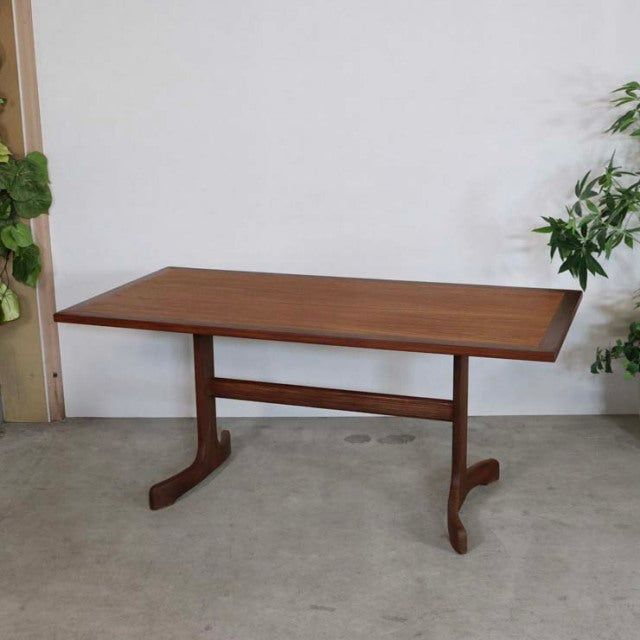 Vintage British mid-century teak dining table with rectangular top and T-shaped legs, showcasing rich wood grain and.
