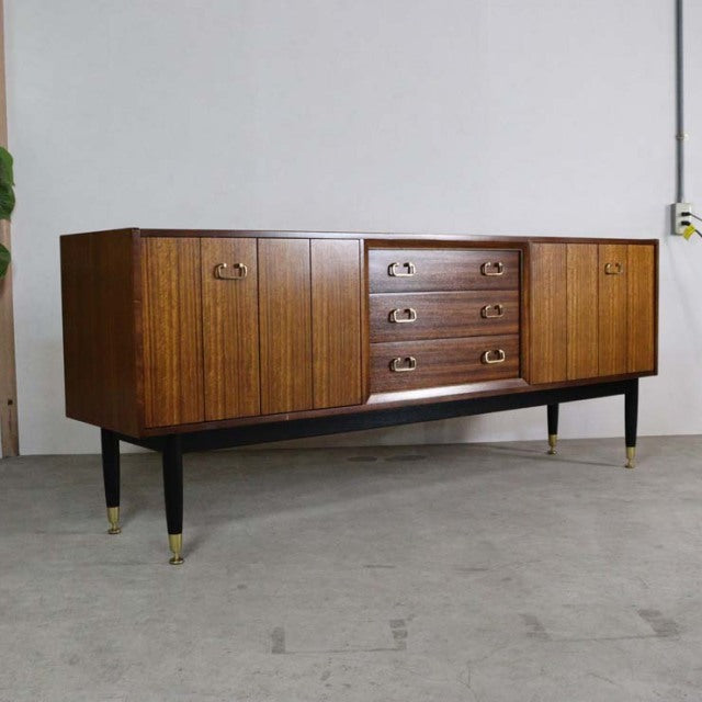 Vintage G-Plan Goldstamp teak sideboard with rich wood grain, brass handles, tapered black legs with brass caps, mid-century .