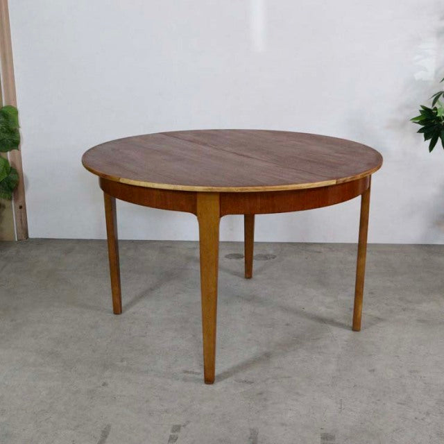 Round mid-century British vintage teak dining table with tapered legs and smooth wood grain finish.