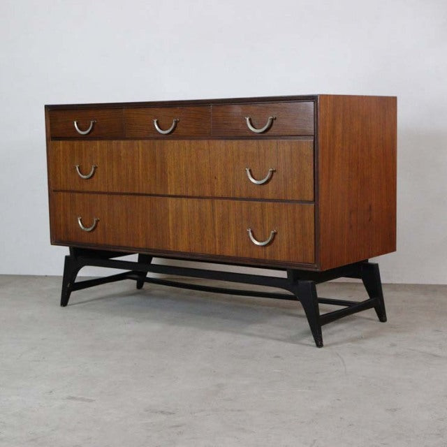 Mid-century British vintage teak chest with three drawers, curved metal handles, and black tapered legs from Meredew.