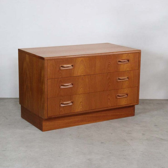 Vintage G-plan mid-century teak chest of drawers with three wide drawers and curved wood handles on short block base.