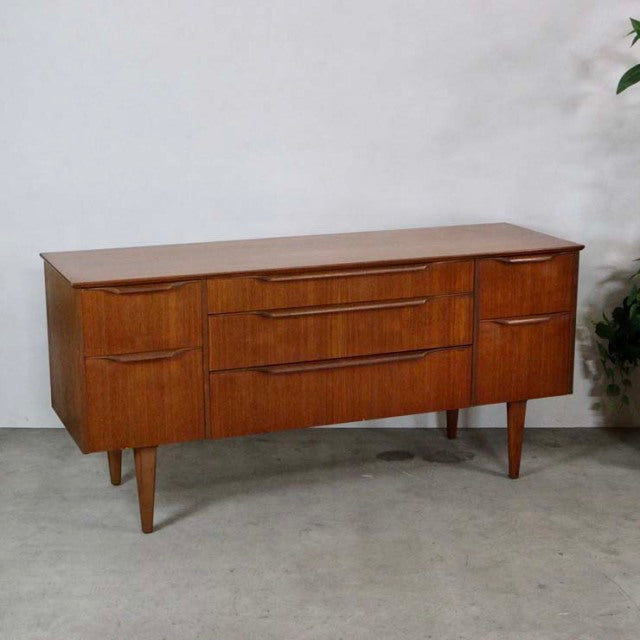 Mid-century British vintage teak sideboard with rich wood grain, tapered legs, and curved drawer fronts.