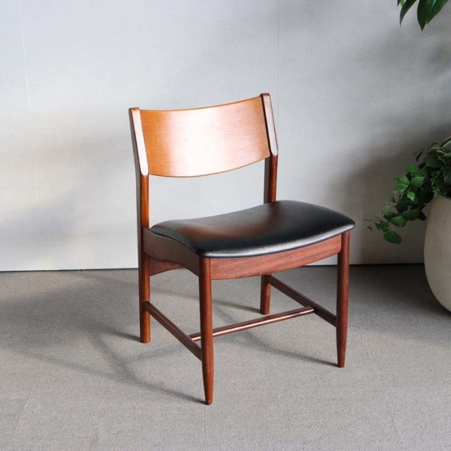 Vintage British mid-century dining chair in rich teak with smooth wood grain, curved backrest, and black leather seat.