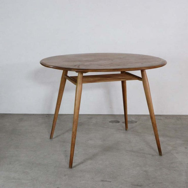 Vintage British mid-century teak dining table with round top, tapered legs, and visible wood grain.