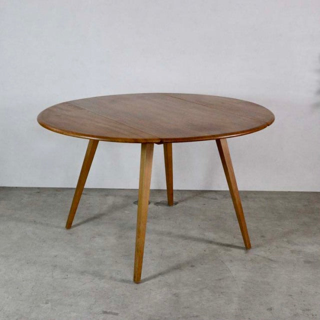 Mid-century British vintage Ercol round dining table in teak with smooth wood grain and slender tapered legs.