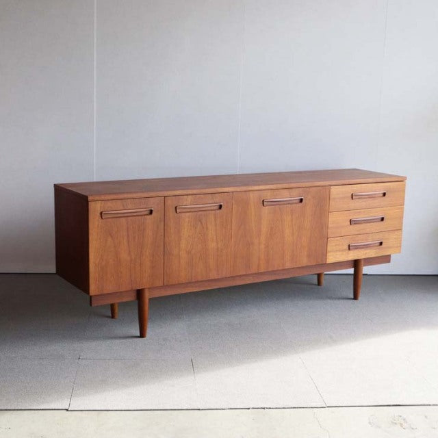 Mid-century British vintage teak sideboard with rich wood grain, four doors, three drawers, and tapered legs.