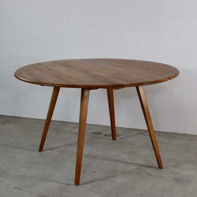 Vintage British mid-century ERCOL dining table in teak with round drop-leaf top and tapered legs.