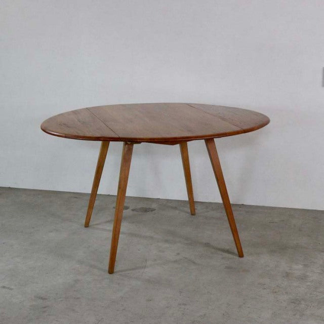 Vintage British Ercol mid-century teak drop-leaf dining table with round top and tapered legs.