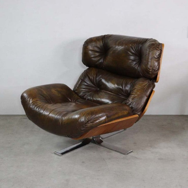 Vintage mid-century British leather armchair with tufted cushions, teak frame, and polished metal swivel base.
