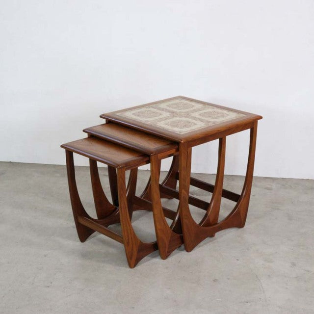 Set of three vintage British mid-century teak nest tables with curved legs and decorative tile tops, showcasing clean wood.