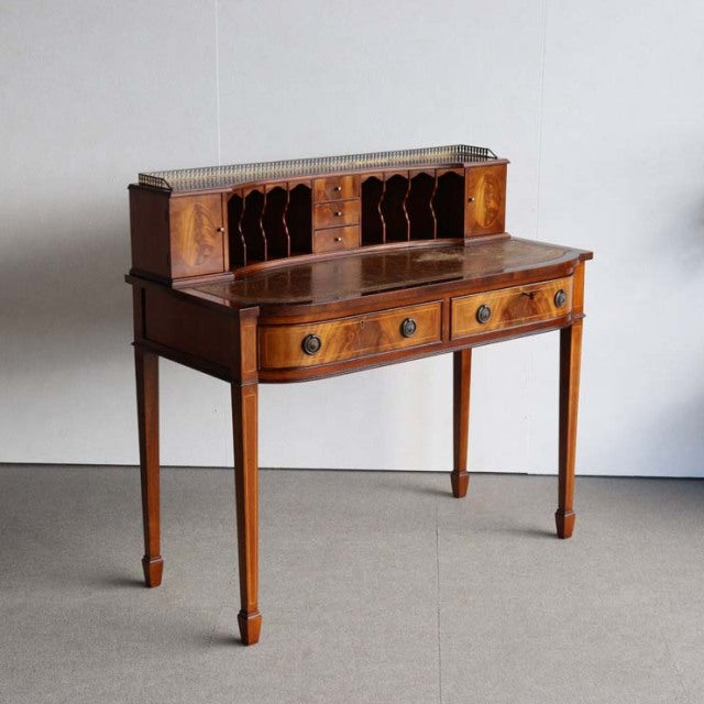Vintage mid-century British teak desk with intricate wood grain, slender tapered legs, and upper cubbyholes for storage.