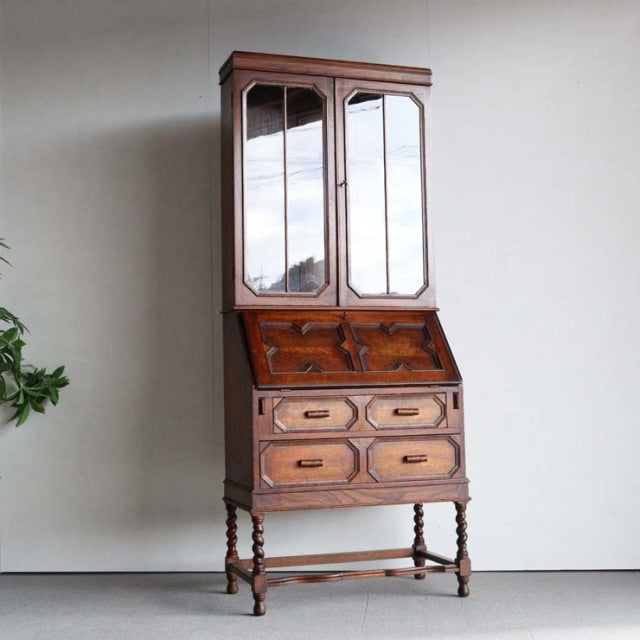 Vintage 1930s British teak cabinet with mirrored doors, drop-front desk, ornate turned legs, and rich wood grain.