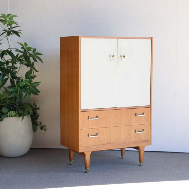 Vintage mid-century British G-Plan teak cabinet with white doors, two drawers, and tapered legs.