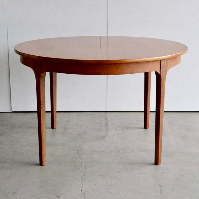 Vintage mid-century British teak dining table with round top, smooth wood grain, and slender tapered legs from Denmark.
